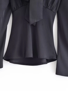 Detail of black long sleeve blouse featuring tie-neck design and flared cuffs in satin finish