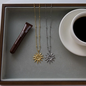 Detail of sun pendant necklace with spiral pattern on velvet tray with coffee