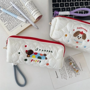 Close-up of quilted pencil cases with cute puppy embroidery on desk with stationery