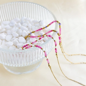 Detailed view of colorful natural stone beads and 18K gold chain in a glass bowl