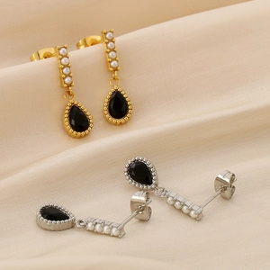 Détail de boucles d'oreilles goutte avec gemmes noires et perles sur satin couleur champagne