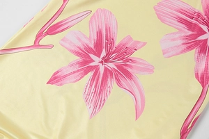 Detail of pink lily floral print on smooth yellow fabric with a silky texture and sheen