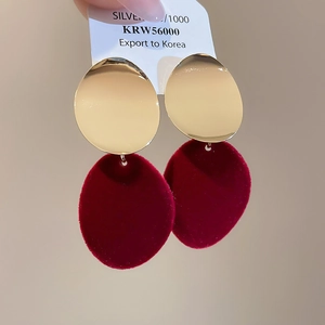 Gros plan de boucles d'oreilles ovales en métal doré et velours rouge sur carte de bijoux