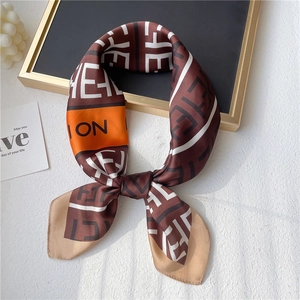Detailed close-up of a satin square scarf with orange stripes and letter patterns