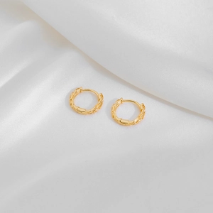 Detailed macro view of gold-plated geometric textured hoop earrings on white silk fabric