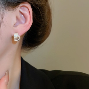 Macro detail of silver brushed metal double C-shaped earrings on a model earlobe