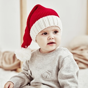Detail of red and white knit Christmas hat with soft white pompom on a baby