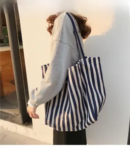 Close-up of a large blue and white striped canvas tote bag worn by a model in soft sunset light