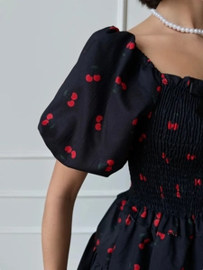 Detail of square neck puff sleeve dress featuring smocked chest and cherry print pattern