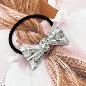 Detail of silver alloy bow knot hair tie with black elastic band on hair texture background