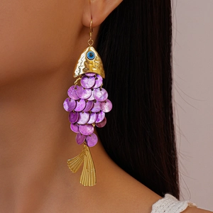 Close-up of golden fish earrings with purple shell scales worn by a model