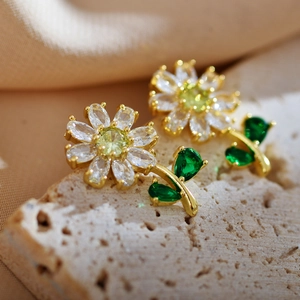 Macro shot of gold plated daisy flower earrings with green and clear faceted gemstones