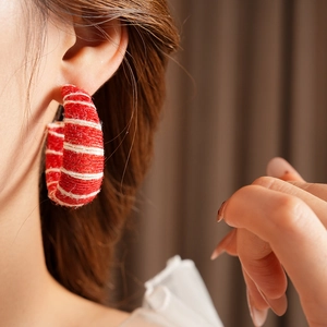 Close-up of red and white striped woven C-shape earring worn by a female model