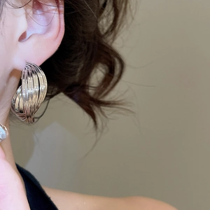 Close-up of a model wearing twisted silver hoop earrings with a sleek metallic finish