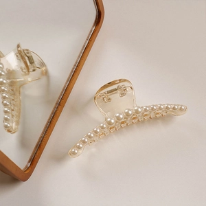 Detail view of champagne acrylic hair claw clip with elegant white pearl embellishments