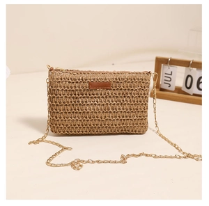 Detail of khaki straw crossbody bag with golden chain strap and leather label on desk