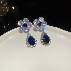 Detailed shot of sparkling zircon flower earrings with blue pear-shaped drop pendants