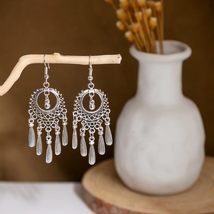 Detail of vintage silver boho earrings with metal tassels hanging on a wood branch