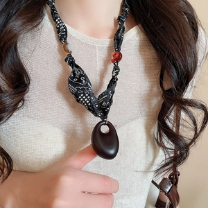 Detailed shot of ethnic fabric necklace with wood pendant on model wearing knitwear