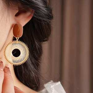 Detail shot of golden circular drop earrings with beige woven texture on female model