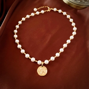 Detailed view of pearl necklace with gold coin portrait pendant on brown satin fabric