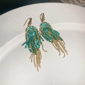 Close-up of long gold chain tassel earrings with green rhinestones on ceramic tray
