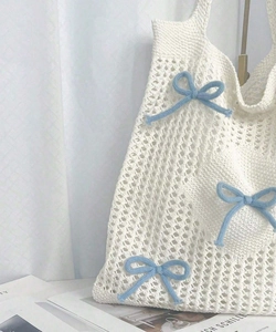 Detail of crochet tote bag featuring blue knitted bows on off-white woven texture