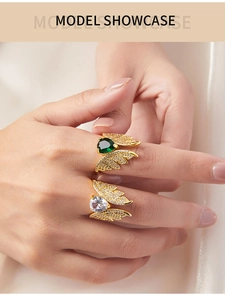 Detail of copper angel wing rings featuring emerald and clear heart-shaped cubic zirconia