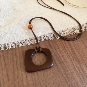 Detail of dark brown resin square pendant necklace with amber bead on wood surface