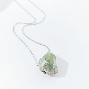Detail view of large raw light green natural crystal pendant on silver necklace