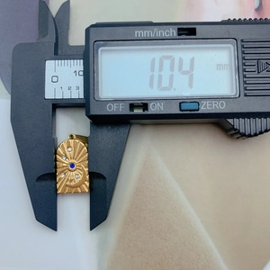 Caliper measuring a gold sun and star pendant with blue gemstone inlay, 10.4 mm height
