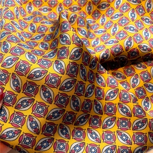 Close-up of 70cm square silk scarf showing geometric eye patterns on yellow fabric