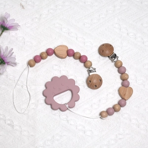 Pink silicone and beech wood baby pacifier clip with flower teether on white knit fabric
