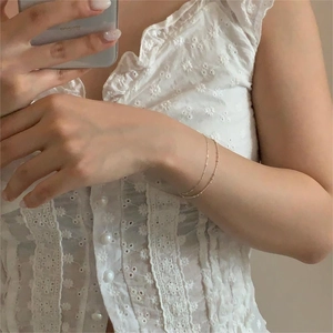 Detailed view of delicate gold beaded layered bracelets worn with a white lace shirt