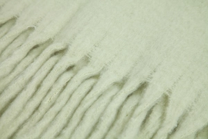 Close-up of soft green mohair scarf fabric with detailed fringe and plush texture