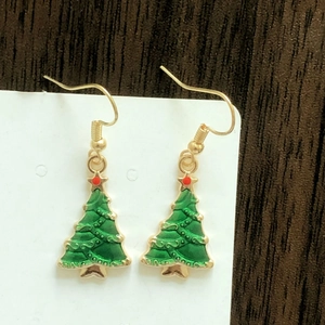 Detail shot of green Christmas tree earrings with gold finish and red dots on wooden surface