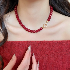 Detail of red acrylic beaded necklace with a gold-plated zircon pendant on a red sweater