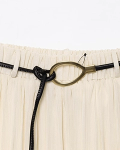 Détail d'une fine ceinture noire en similicuir avec boucle dorée sur jupe plissée beige