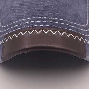 Makroaufnahme der blauen Denim-Baseballkappe mit braunem Lederbesatz und weißer Naht