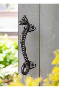 Detail of vintage seahorse cast iron door handle mounted on gray wooden frame