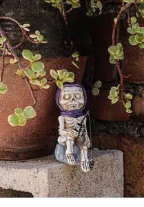 Detailed resin skeleton figurine with purple cloak fishing on a rock base in a garden setting