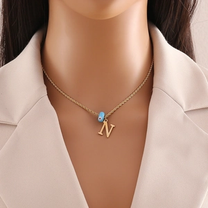 Detail view of gold twisted chain with letter N pendant and blue evil eye charm on model
