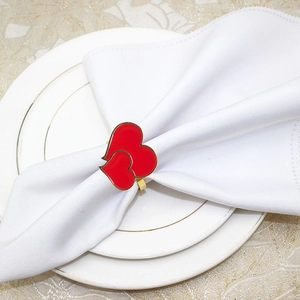 Detail of red enamel double heart napkin ring with gold trim on white napkin