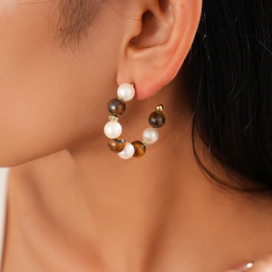 Detail of 16K gold plated C-shaped earrings with tiger eye beads and pearls on model