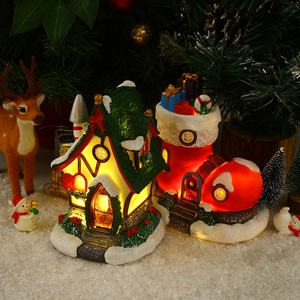 Close-up of lighted resin Christmas snow house and gift boot ornaments on snow