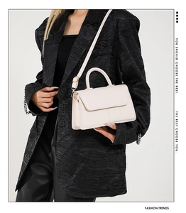 Close-up of a white textured leather crossbody bag styled with a black blazer
