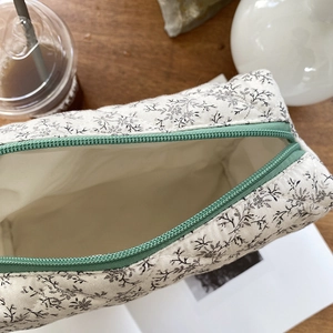 Detail of floral quilted cosmetic bag with green zipper on a wooden table surface