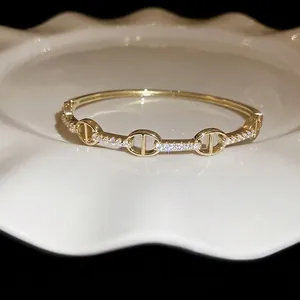Gold plated oval bangle with cubic zirconia stones featuring a designer link pattern