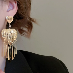 Macro shot of large golden heart earrings with hammered texture and long metallic tassels