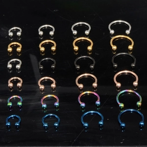 Multiple sizes and colors of C-shape stainless steel piercing rings on black background